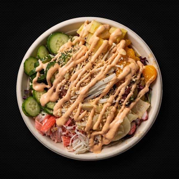 Top-down view of a poke bowl with cucumbers, pineapple, mandarins, crab, and spicy mayo.