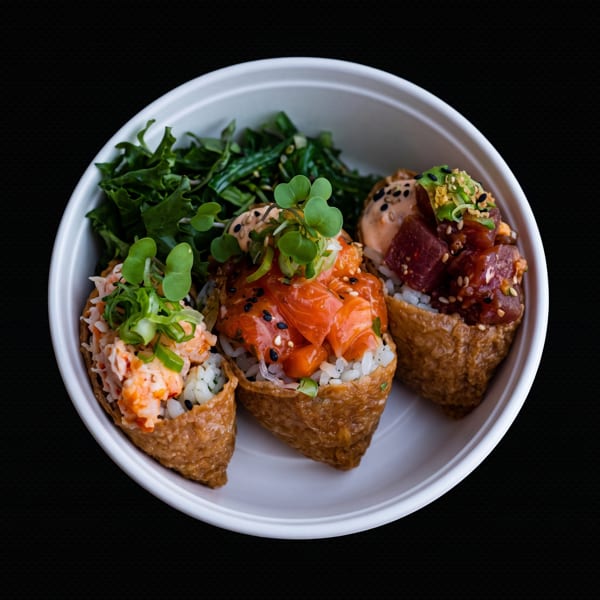 Three inari sushi with various toppings and a side of greens in a white bowl.