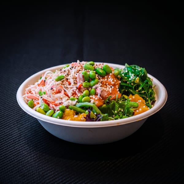 A colorful poke bowl with crab, edamame, salmon, seaweed, and greens in a white bowl.