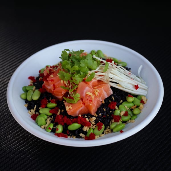 Salmon poke bowl with black rice, edamame, red roe, enoki mushrooms, and cilantro.